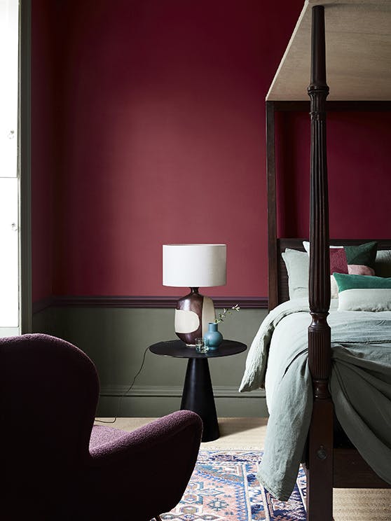 Deep red (Baked Cherry) bedroom with a contrasting dark green lower wall behind a four poster bed and armchair.