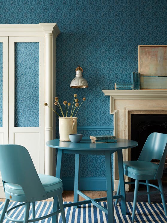 Dining space with a tonal blue wallpaper (Hoja - Air Force Blue) and white (Shirting) cupboard with blue table and chairs.