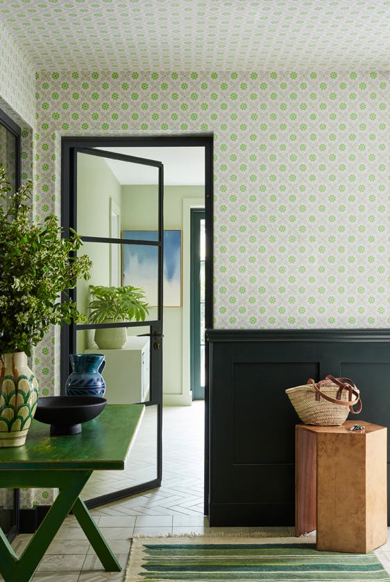 Close up of the grey and green small print floral wallpaper 'Ditsy Block - Phthalo' on a wall with a dark green panel below and a plate on top.