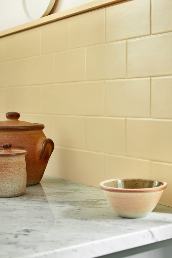 Close-up of light yellow kitchen tiles painted in 'Sunlight' alongside marble kitchen units.