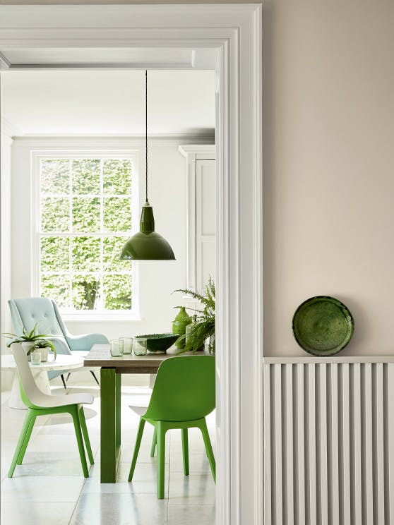 Hallway looking into a dining room painted in beige shade Portland Stone - Dark with bright green dining room chairs.