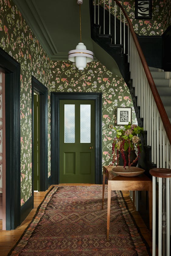 High ceiling hallway featuring dark green floral wallpaper (Aderyn - Olive Colour) with dark green woodwork and a tapestry rug.