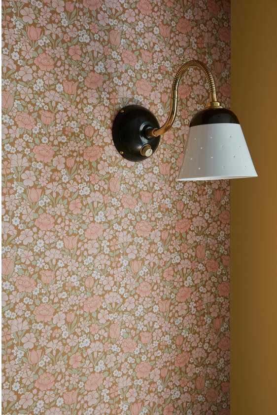 Close up of the golden brown and pink floral wallpaper 'Spring Flowers - Bombolone' on a wall with a wall light.