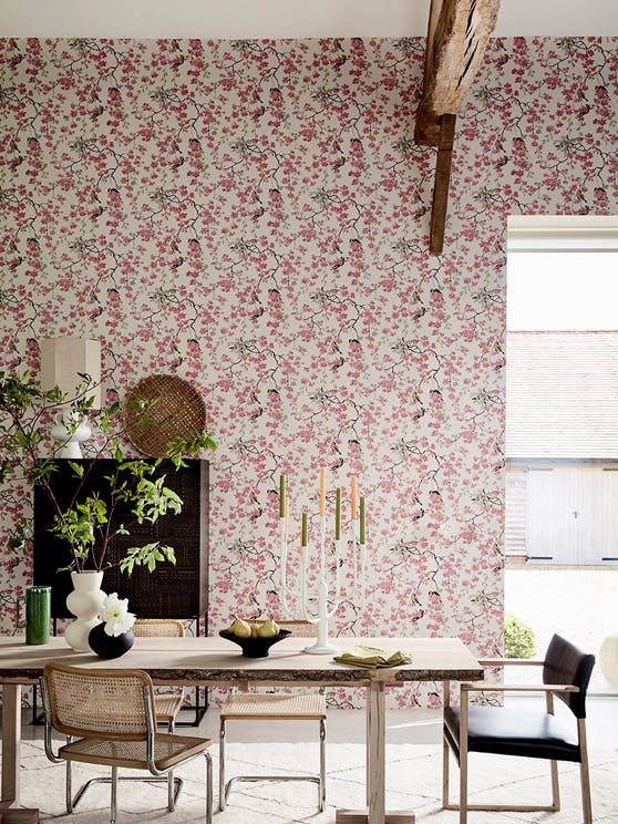 Dining room with pink printed floral and bird wallpaper (Massingberd Blossom - Mineral) and wooden dining table and chairs.