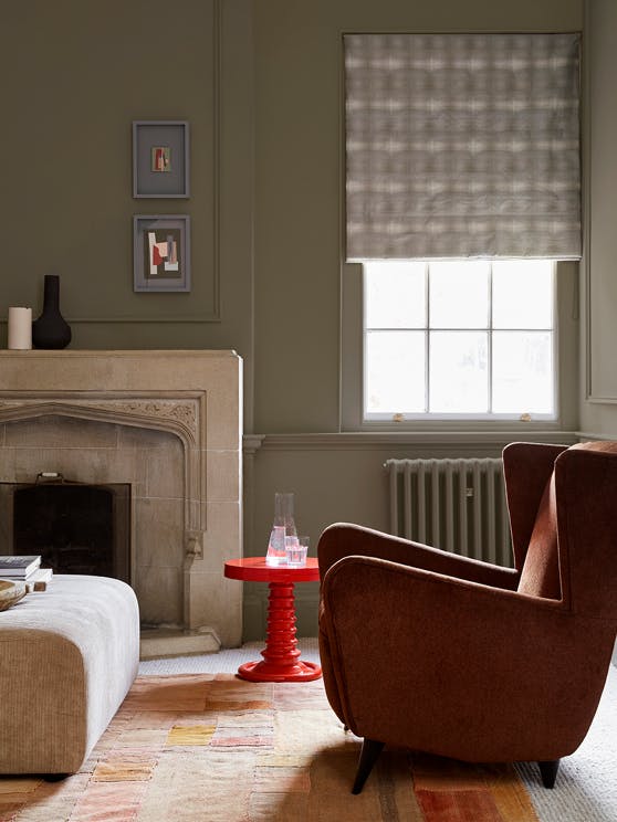 Living space with grey neutral walls (Baluster) alongside a fireplace, armchair and a bright red coffee table.