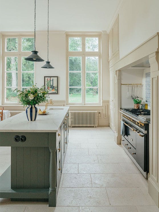 A kitchen featuring a grey island, walls painted in various Clay tones and two large windows overlooking a garden.