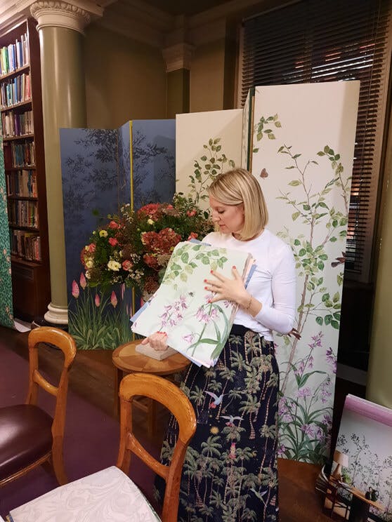 Woman (Ruth) showcasing the National Trust Papers III samples in front of a large wallpaper display.