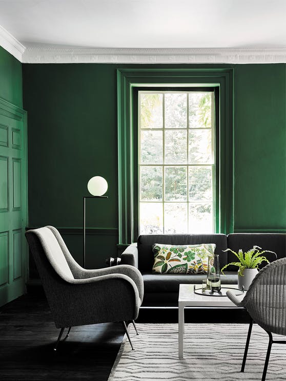 Living space painted in dark green (Puck) with a grey sofa, armchair and a white table on a rug.