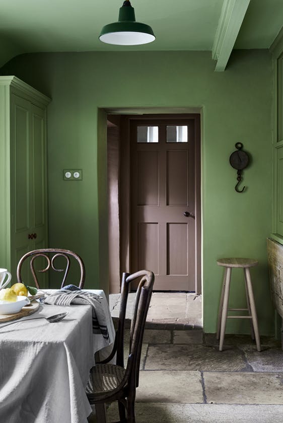 Deep green (Garden) dining space with contrasting brown door and a dining room table with chairs.