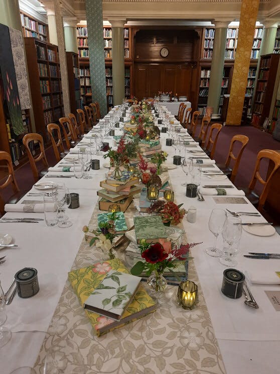 Long table inside a library decorated with a Briar Rose table runner and wallpaper-covered books as centrepieces.