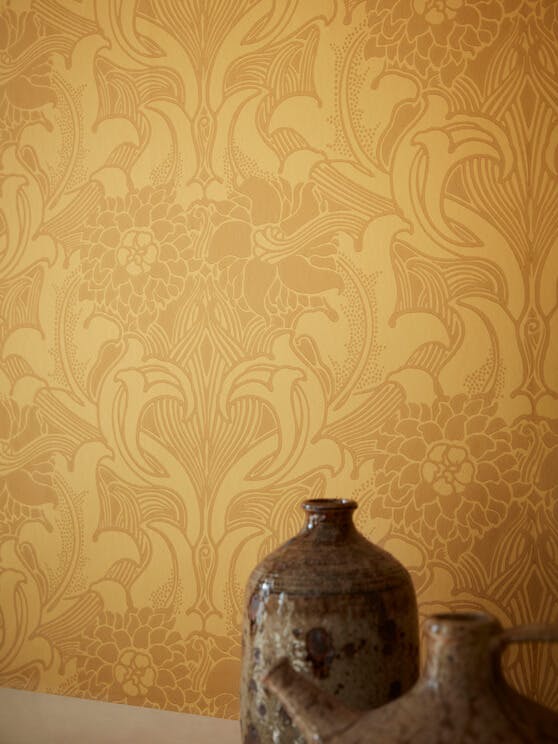 Close-up of National Trust yellow floral wallpaper (Dahlia Scroll - Giallo) with two brown ornaments in the right corner.