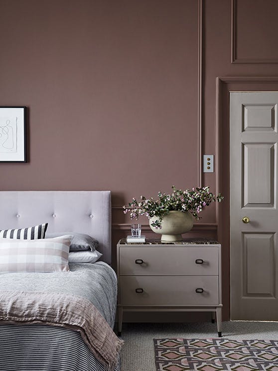 Bedroom painted in warm red (Nether Red) with contrasting grey woodwork and a bed scattered with cushions.