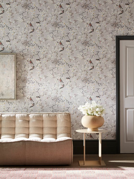 A buttoned sofa and side table in front of a wall decorated with flower and bird themed wallpaper (Massingberd - Grey).