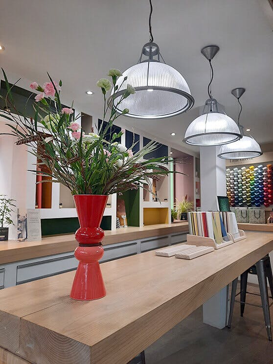 Long wooden table with a red vase and flowers and colour samples on top inside the Little Greene Paris showroom.