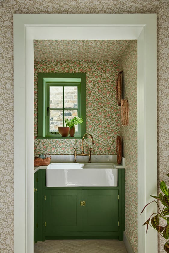 Pantry featuring two colourways of the floral wallpaper 'Spring Flowers' with dark green woodwork and a window above a sink.