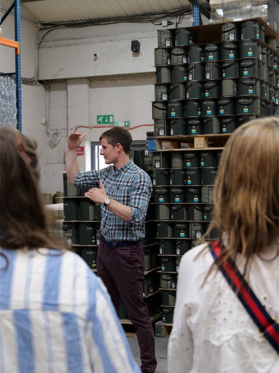 Man standing in front of Little Greene paint tins stacked on shelves in a warehouse.