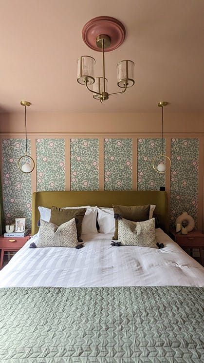 Bed with green and white cushions and bedding in front of a wall featuring pink panelling and Briar Rose - Salix wallpaper.