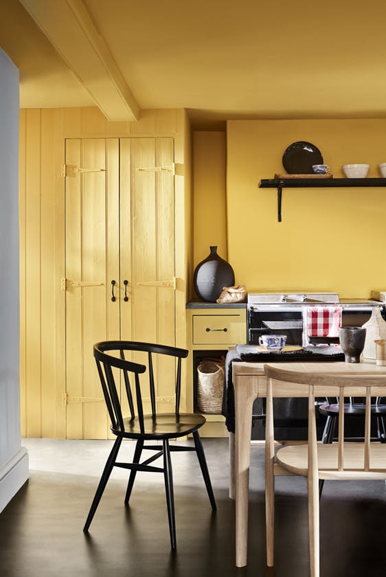 Kitchen color drenched in vibrant yellow shade 'Giallo', with a wooden table and chairs.