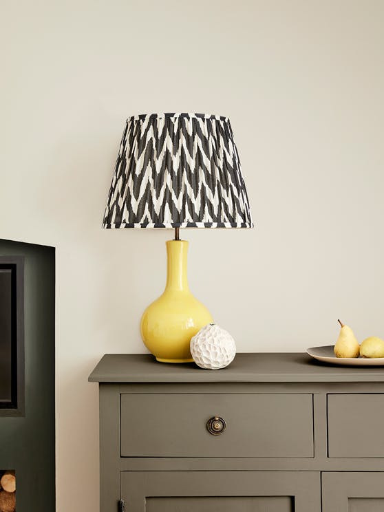 Close-up of a neutral wall in Portland Stone, behind grey-brown drawers (Baluster) topped with a yellow and dark grey lamp.