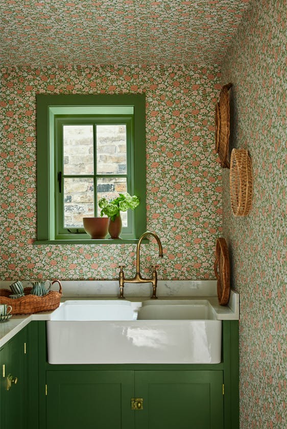 Pantry with a the green and pink small print ditsy floral wallpaper 'Spring Flowers - Garden' on the walls and ceiling with dark green woodwork and a window above a sink.
