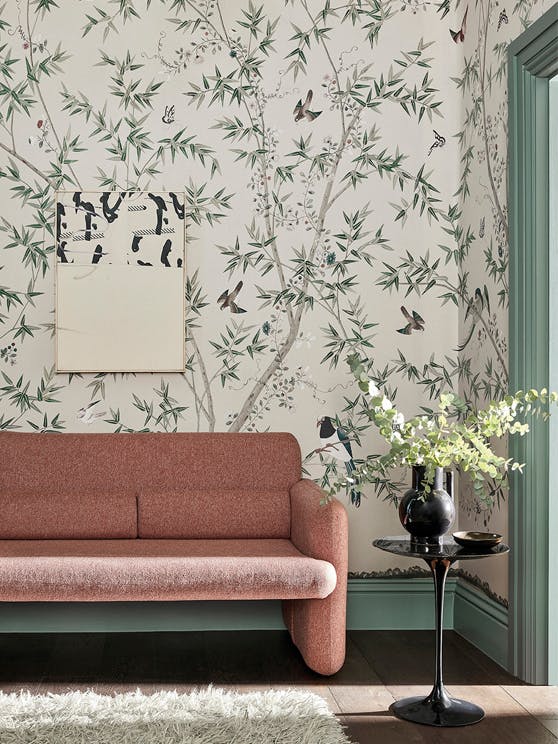 Living room with mural wallpaper featuring birds, butterflies and flowers, a muted red couch and dark green baseboards.