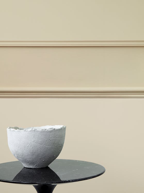 Close-up of a paneled wall in different shades of warm neutral 'Travertine', behind a black table with a white bowl on top.