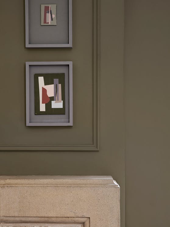 Two pieces of abstract artwork hung vertically on a grey neutral wall, painted in Baluster, above a stone colored fireplace.