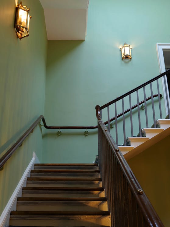 Brown staircase going up inside the Horse Guards building with bespoke pea green (Horse Guards Green) painted walls.