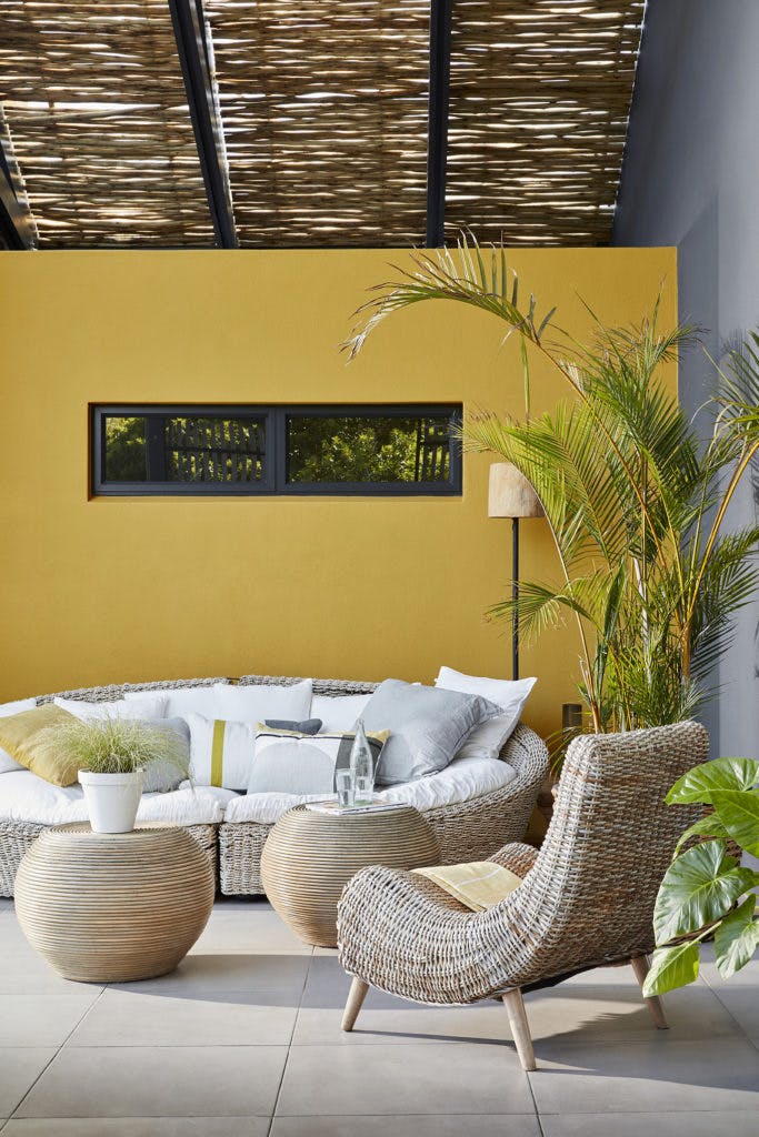 Outside seating area with a large wicker sofa and chair with a bright yellow wall (Yellow-Pink).