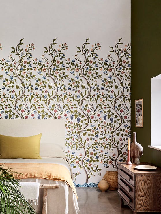 Bedroom with off white floral mural wallpaper (Mandalay - Ceviche) with a bed, sideboard and plant.
