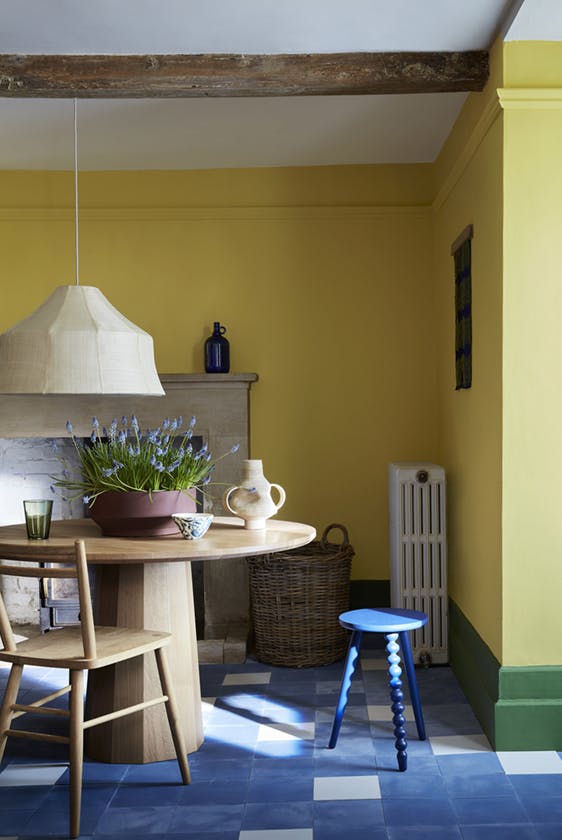 Dining room with vibrant yellow walls (Indian Yellow) with a green baseboard and wooden table and chairs.