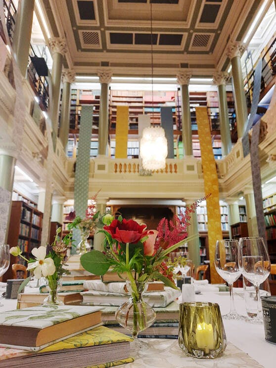 A dining table featuring books and flowers as centerpieces with a tall two-storey library visible in the background.