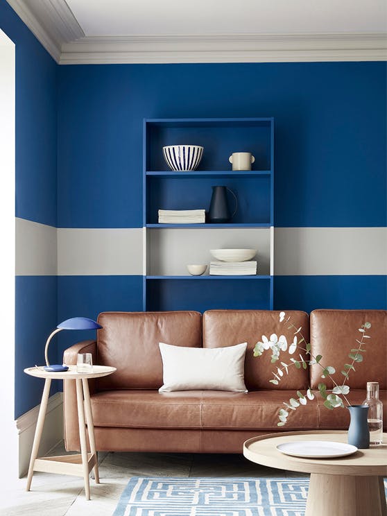 Living space with rich blue (Mazarine) wall and a contrasting neutral (Cool Arbour) stripe with a tan leather sofa.