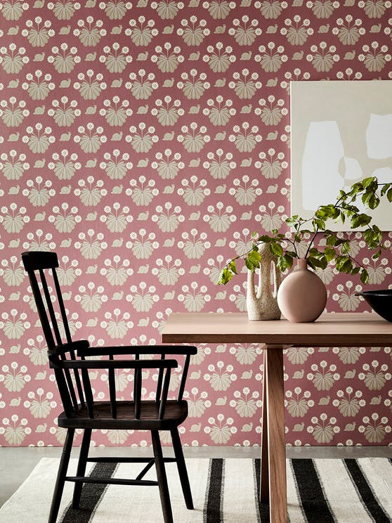 Dining room with pink printed snail wallpaper (Burges Snail - Rosie) behind a wooden dining room table and chair.