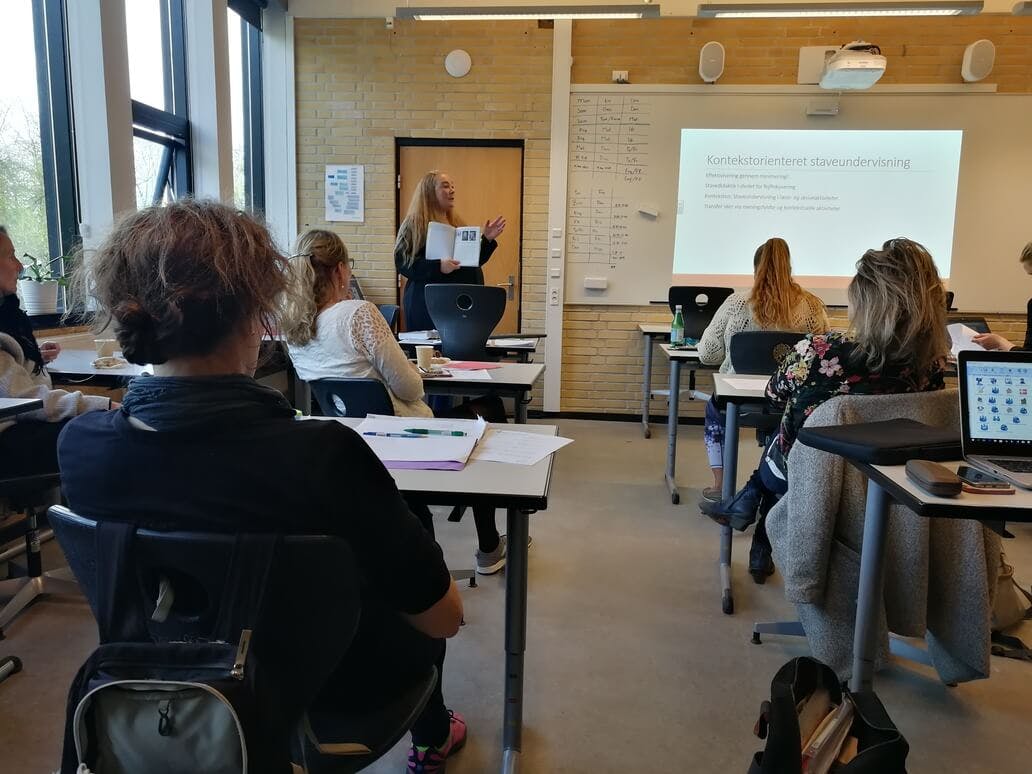 Et klasseværelse med elever og en lærer ved tavlen