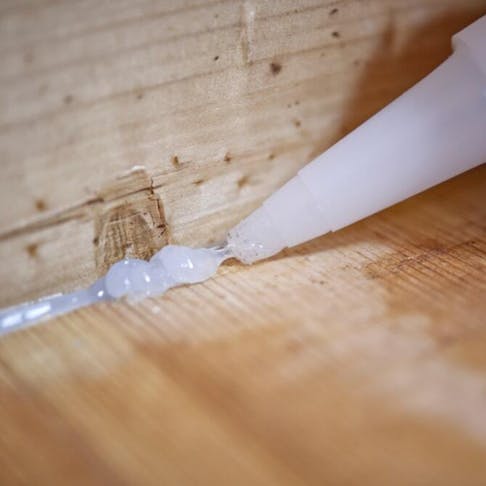 Applying silicone to gap between wood floor and wall. Image Credit: Nikox2/Shutterstock.com