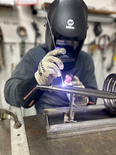 An engineer at Aqua Logic TIG welding titanium fitting to a titanium coil.