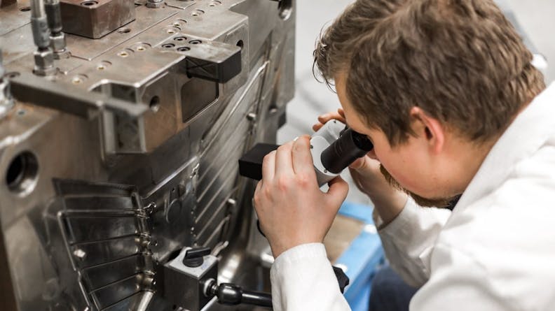 Injection mold being inspected using a microscope.
