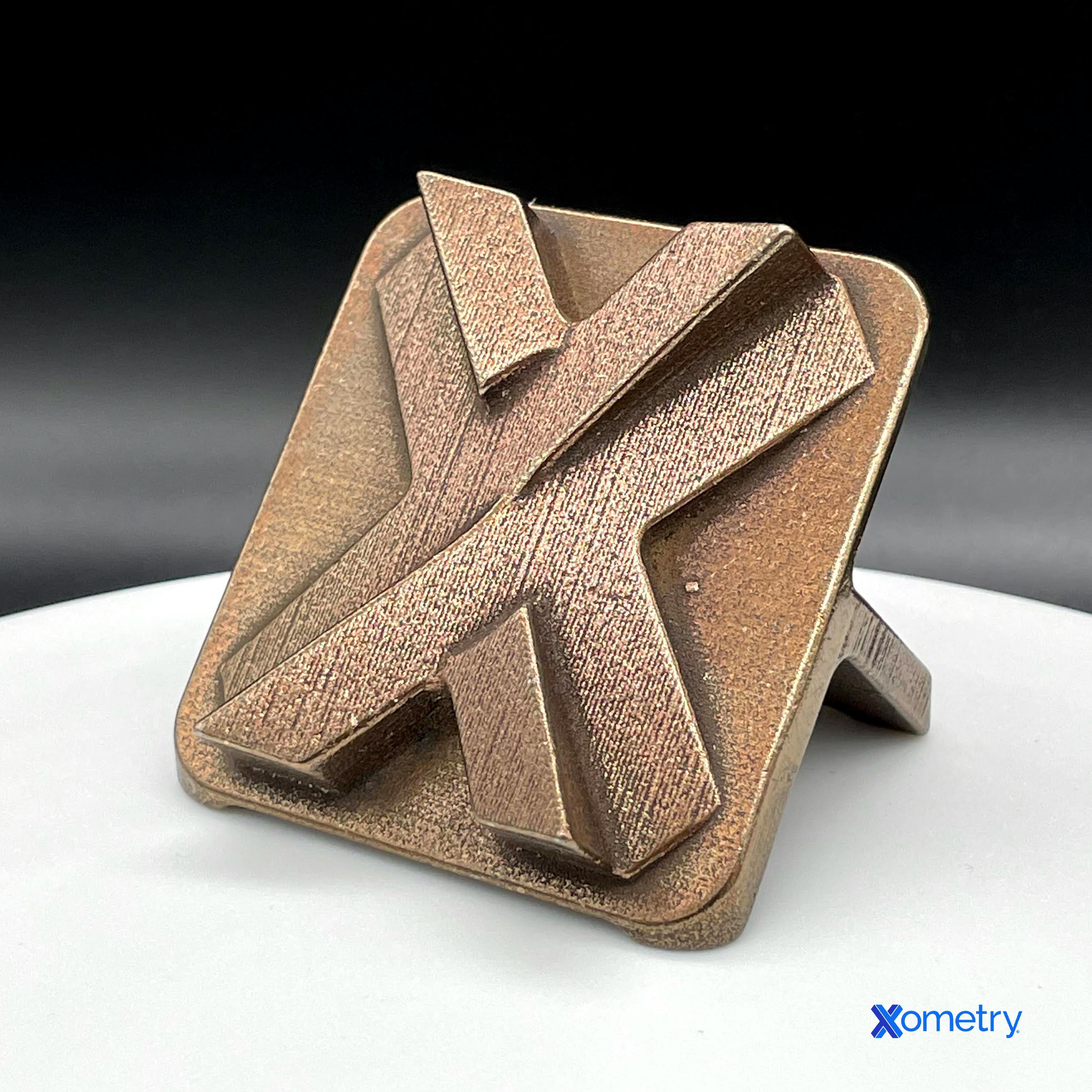 A Xometry logo with bronze infill