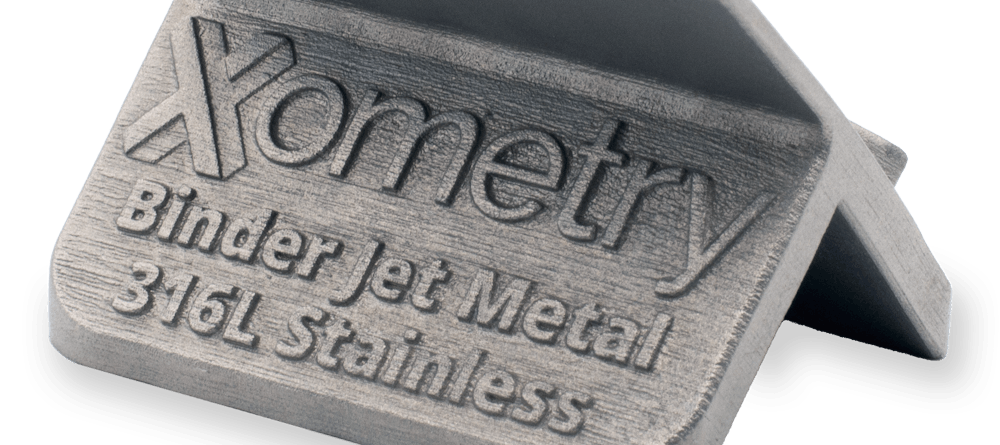 The back of a 316L stainless steel binder jet printed Xometry tile showcasing text.