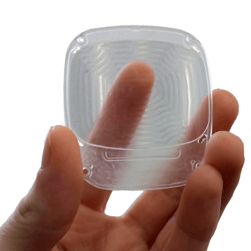 A machined part made of clear polycarbonate being held.