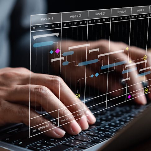 Close-up of hands typing on a laptop displaying a scheduling program