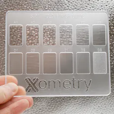 Injection molded finishes card in clear polycarbonate being held against a textured background.