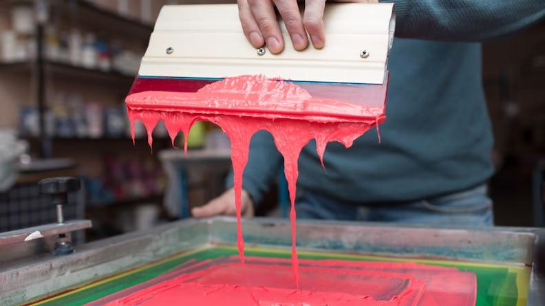 A person using an ink blade to prepare a silk screen for printing.
