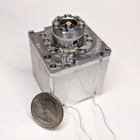 a picture of a pico satellite thruster, with a quarter leaning against it for size comparison