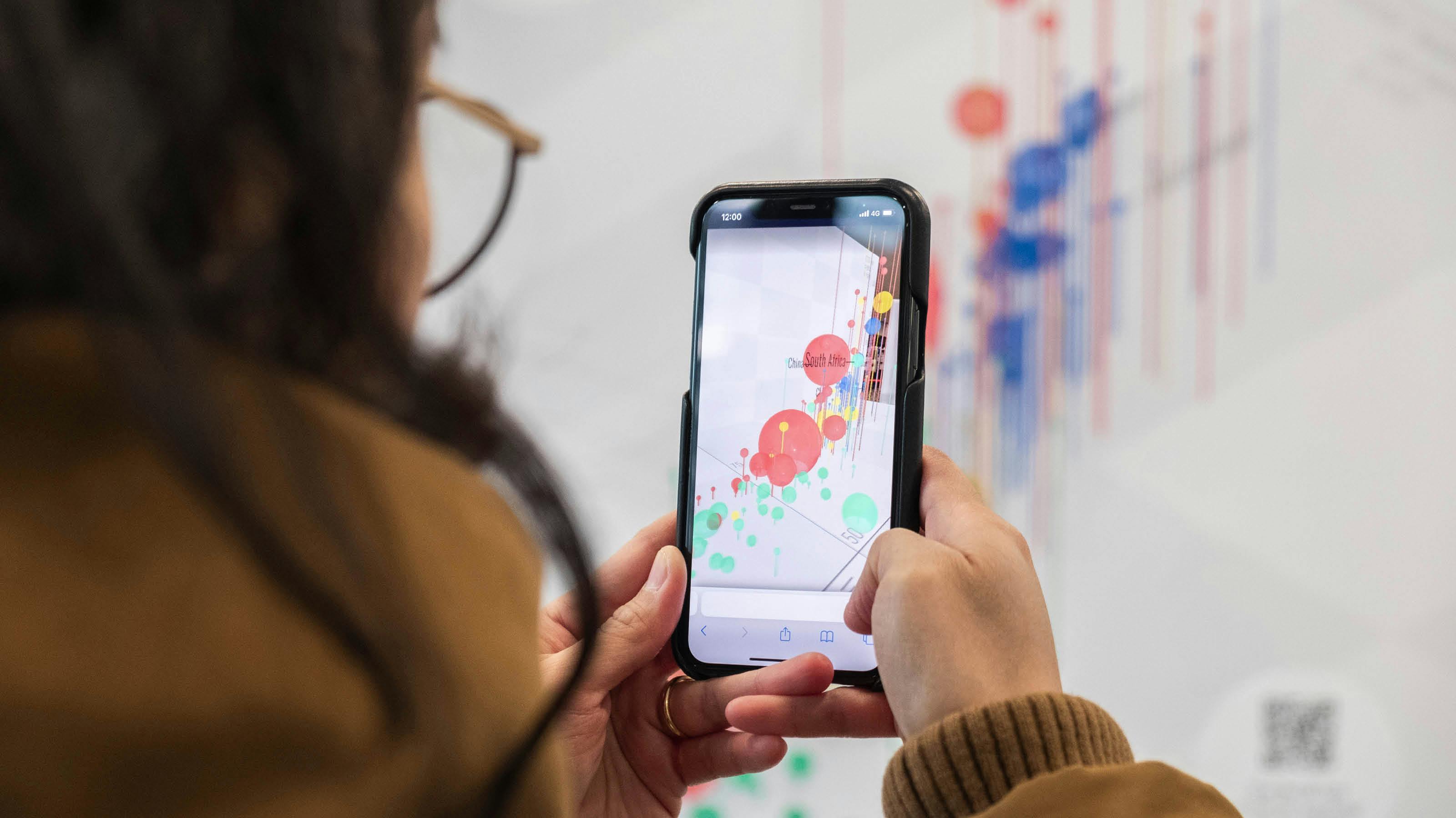 In the image, a person is holding an iPhone to take a photo of a white board with colorful dots and lines on it.