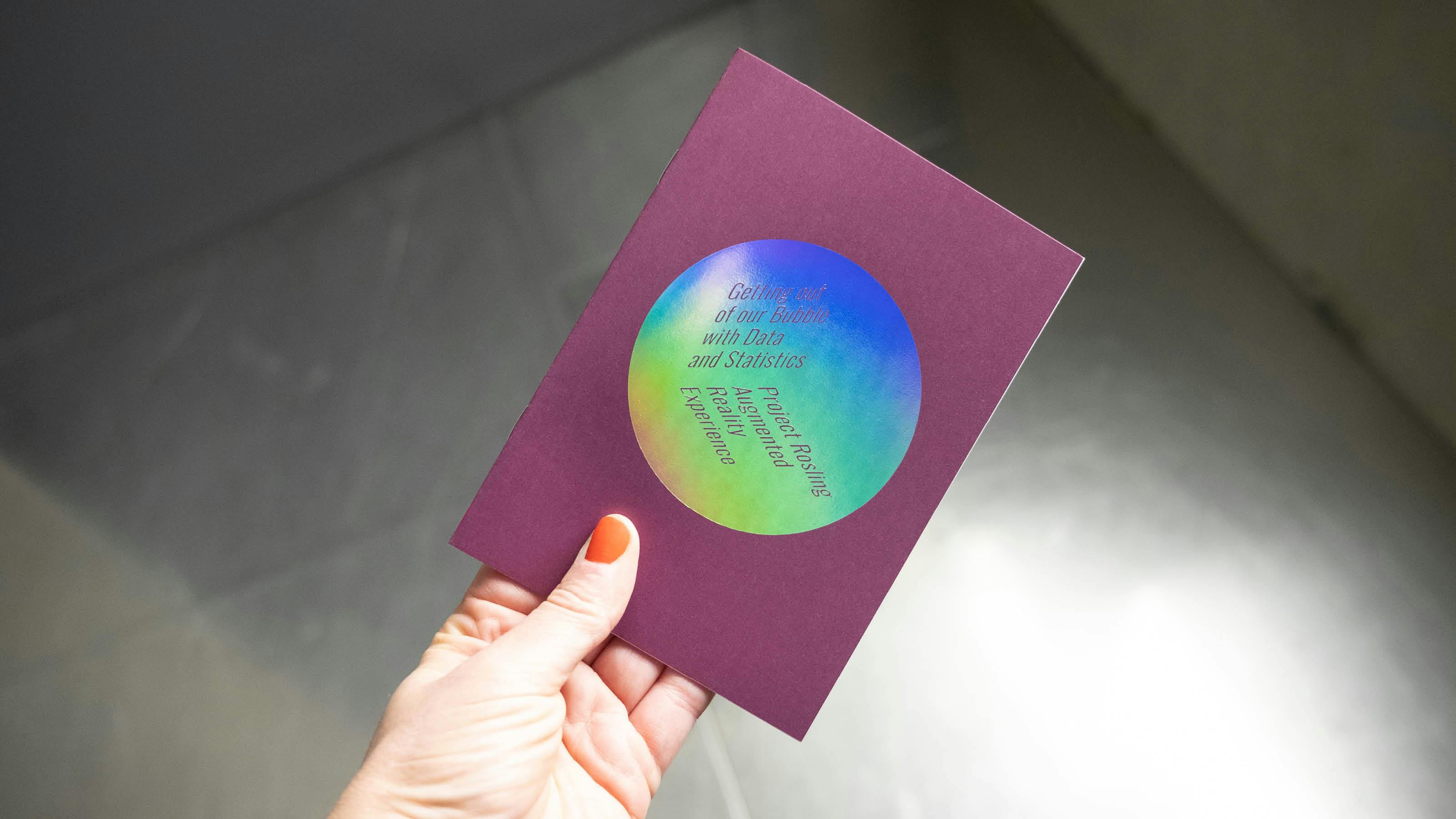 A hand with orange nails holds a purple card with a rainbow-colored circle that says \"Getting out of our Bubble with Data and Statistics\" 