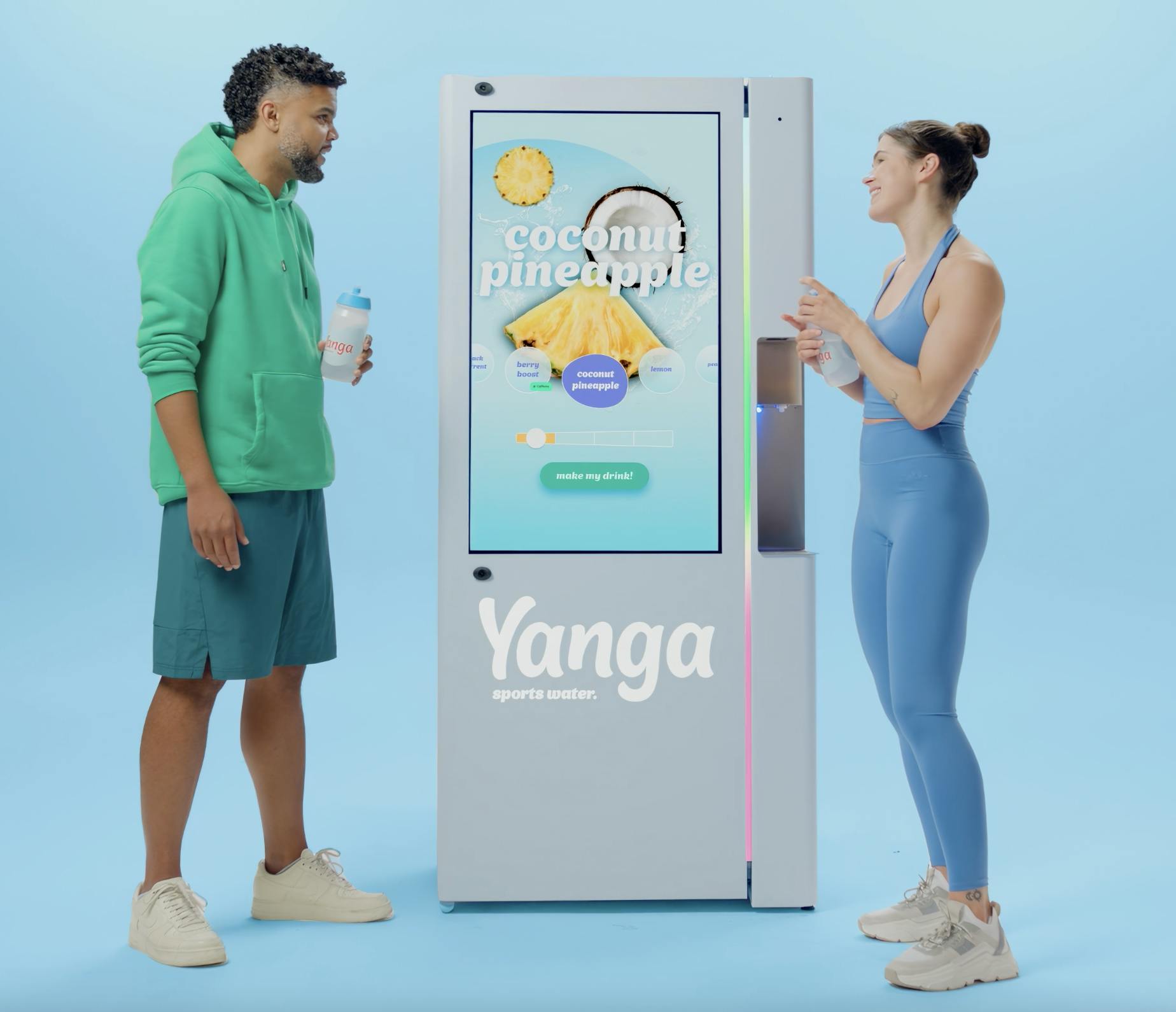 Two people stand smiling and holding water bottles in front of a Yanga sports water hydration station.