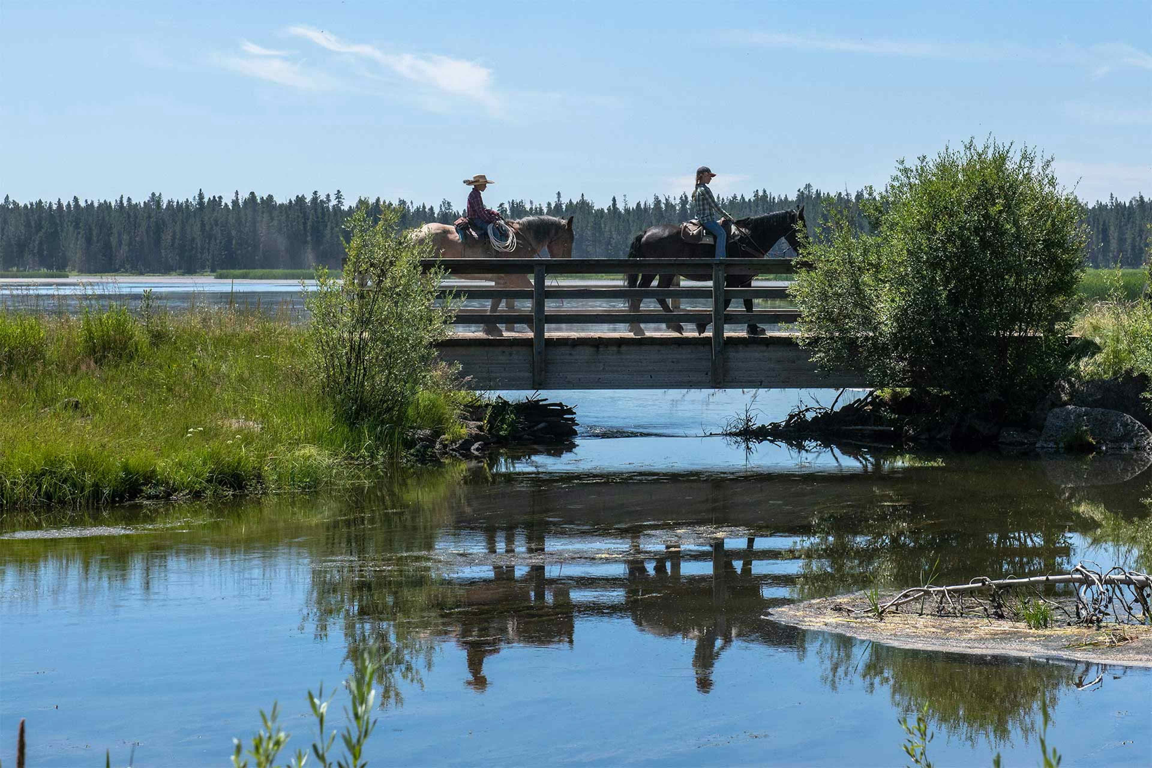 Two horseback riders cross a bridge over Silver Lake at Harriman State Park, Island Park ID.
