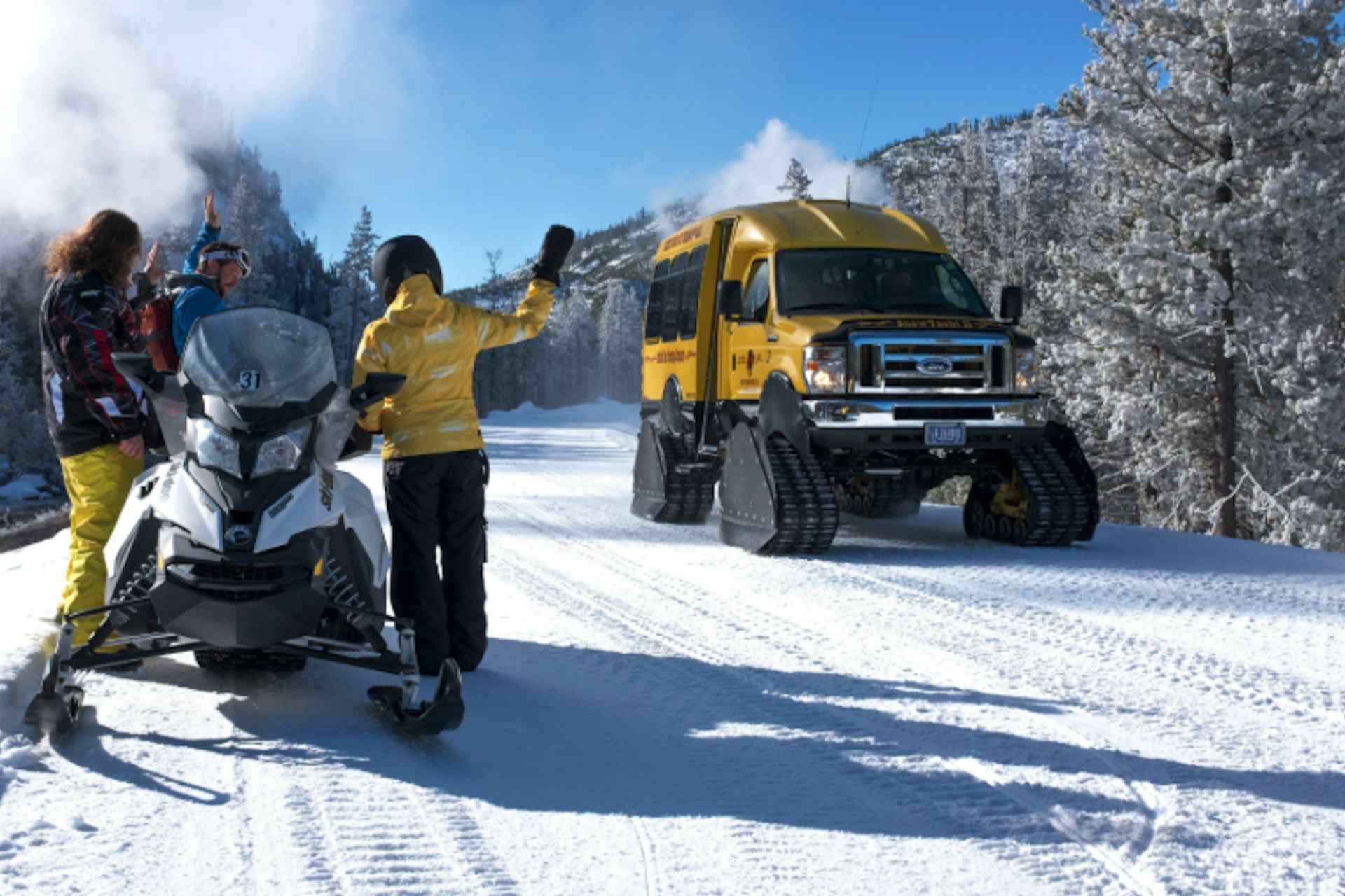 image of a snow machine with 2 people being passed by a snow coach in yellowstone national park in winter.